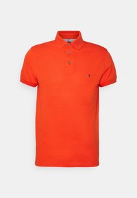 Ljust orange kortärmad polo med tre knappar och liten logotyp på vänster bröst mot vit bakgrund.