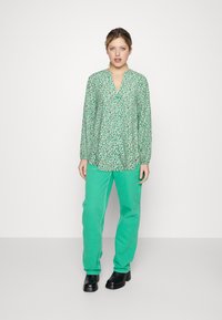 Groen gestreepte blouse met een V-halsontwerp en lange mouwen, gecombineerd met groene broek en zwarte haklaarzen.