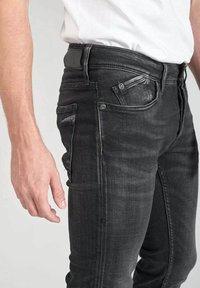 Vaqueros de mezclilla negros con un corte ajustado, cinco bolsillos, desvanecido sutil, costuras decorativas y cierre de botón en la cinturilla.