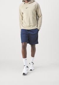 Beige huvtröja med texturdetailler, marinblå shorts, vita strumpor och svart-vita sneakers. Nike-logotyper finns på alla artiklar.