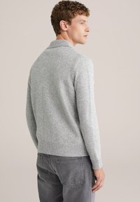 Grå stickad tröja med ribbad krage och ärmslut. Mjuk textur, medelpassform, kort nederkant och sömlös axeldesign. Bärs med mörkgrå byxor.