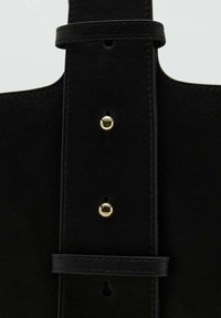 Detalle de bolso de cuero negro con textura suave, correa ajustable, herrajes en tono dorado y costuras a lo largo de los bordes.