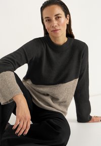 Schwarzer und beiger Farbblock-Pullover aus weichem, strukturiertem Material mit geripptem Saum und Bündchen. Er verfügt über einen Rundhalsausschnitt und eine lässige Passform.