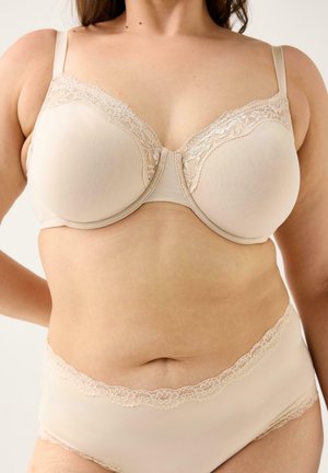 Kvinde iført en beige bh med blondestrimler og matchende trusser med høj talje, der viser maveområdet og naturlig hudstruktur.