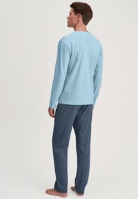 Chemise bleu clair à manches longues avec un col rond, associée à un pantalon marine à motifs présentant un design de vagues, portée par une personne.
