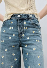 Ljusblå, broderade denimjeans med vita och gula prästkrage-mönster. Midjehög med framfickor och bältesloopar.