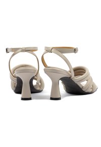 Beige Leder Sandalen mit Absatz, runder Zehenpartie, Knöchelriemen und einem geschwungenen schwarzen Blockabsatz. Verfügt über gedrehte Riemen für zusätzlichen Detailreichtum.
