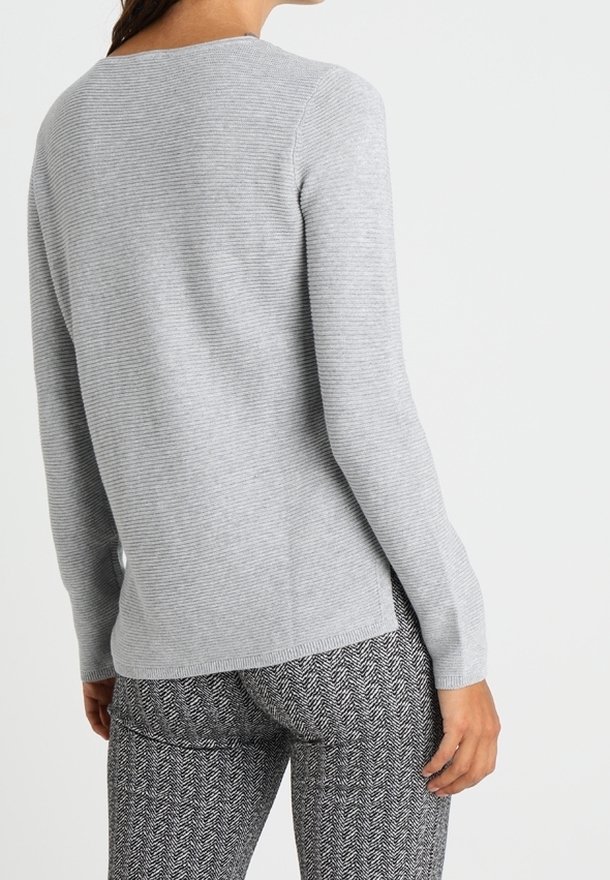 Femme portant un pull côtelé gris clair à manches longues et un pantalon gris motif chevrons, vue de dos et de la taille vers le haut.