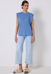 Top azul de manga corta con un corte relajado, combinado con jeans de pierna ancha de lavado claro y pantuflas beiges esponjosas. Apariencia simple y casual.
