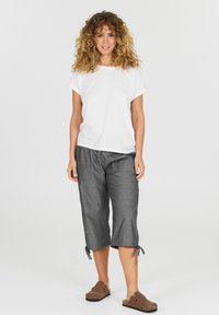 Valkoinen lyhythihainen t-paita, harmaat lyhyet housut sivutaskuilla ja nyörit hemmoissa, yhdistettynä ruskeisiin liukuväliin kenkiin.