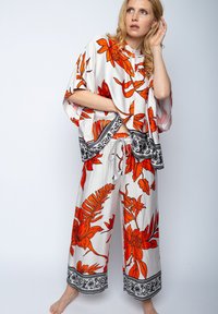 Kwiatowy zestaw składający się z krótkiego rękawa bluzki i szerokich spodni, w kolorze białym z wyrazistymi pomarańczowymi kwiatami i czarnymi wzorzystymi akcentami.