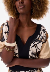 Korte mouw jurk met een V-hals, bloemenpatronen in zwart en bruin, zwarte accenten en een gladde stof. Accessoires omvatten gelaagde armbanden.