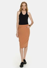 Czarny bezrękawnik w połączeniu z dopasowaną, pomarańczową spódnicą ołówkową do kolan, z boczną kieszenią i gładką fakturą. Proste czarne sneakersy.