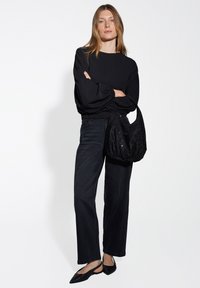 Top nero a maniche lunghe con orlo arricciato, abbinato a jeans scuri a vita alta. Una borsa a spalla nera con paillettes testurizzate e ballerine nere completano il look.