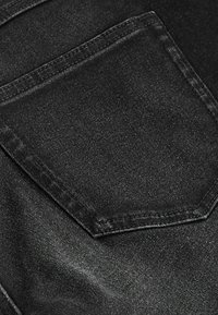 Țesătură din denim negru, arătând o folie posterioară cu cusături contrastante. Textura pare netedă, cu un ușor luciu. Folia are o formă rectangulară.