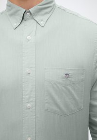 Chemise vert clair boutonnée avec un col boutonné et une poche poitrine présentant un petit logo brodé avec des étoiles et des rayures.