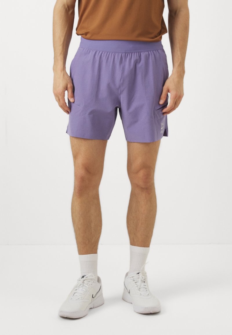 Lila Sportshorts mit einem elastischen Bund, flachen Fronttaschen und einem minimalistischen Logo auf der unteren linken Seite.