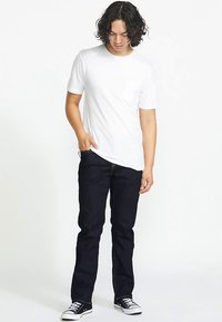 Biała koszulka z krótkim rękawem i kieszonką, zestawiona z ciemnoniebieskimi dżinsami i czarnymi trampkami. Luźny krój, gładka faktura bez widocznych wzorów.