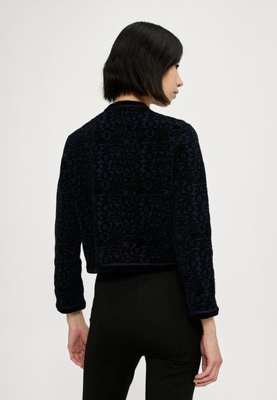 Chaqueta recortada de navy texturizado con mangas largas, que presenta un diseño estampado y un cuello redondo, combinada con pantalones negros ajustados.