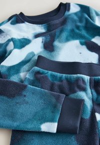 Kék árnyalatú flannel loungewear szett absztrakt mintákkal. A felső kerek nyakú; a nadrág rugalmas derékkal és passzoló mandzsettákkal.