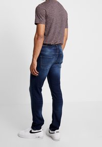 Mörkblå jeans i slim fit med bakfickor och subtila nedsvärtningar. Kombineras med en grå t-shirt med kort ärm och vita sneakers.