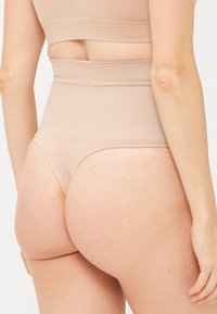 Hochgeschnittene beige Unterwäsche mit glatter Textur, ausgestattet mit einem dehnbaren Bund und einem Design mit minimaler Abdeckung.
