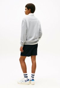 Sudadera gris claro con puños acanalados, acompañada de pantalones cortos azul marino. Zapatillas blancas con acentos en azul y calcetines a rayas azul marino completan el conjunto.