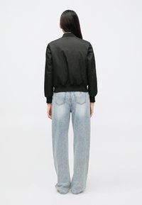 Μαύρο μπουφάν bombers μ�ε ριμπ γιακά και μανσέτες, σε συνδυασμό με ανοιχτό μπλε τζιν παντελόνι με φαρδιά γραμμή, διακοσμημένο με ξεβαμμένες λεπτομέρειες και πίσω τσέπες.