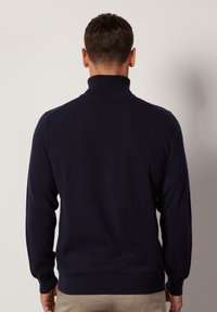 Marinblå stickad tröja med hög krage, ribbade ärmslut och nederkant. Slät textur, figurnära design och en enkel, klassisk look.