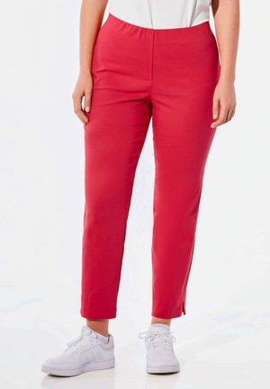 Pantaloni stretchy rossi con vita elastica, taglio aderente, lunghezza alla caviglia, con spacco laterale sull'orlo, abbinati a sneakers bianche.