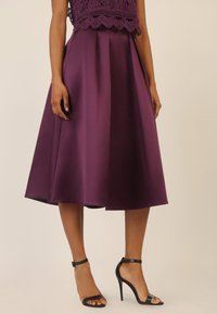 Gonna di raso viola con pieghe, lunghezza fino al ginocchio. Indossata con tacchi alti neri con cinturini. Presenta un top in pizzo, che aggiunge texture e dettagli.