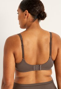 Brun behå med justerbara axelremmar och hak-och-öga-stängning bak. Slät textur och enkel design, lämplig för vardagsbruk.