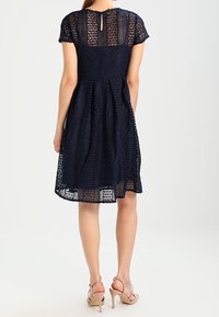 Laivansiniset pitsimekko, jossa on lyhyet hihat, takana avainaukko ja levenevä hame. Siinä on monimutkaisia leikkauksia ja vuorattu sisustus.