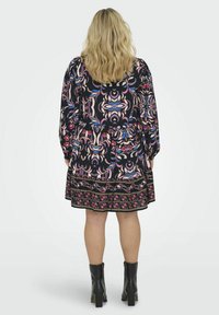 Abito nero a fantasia floreale con maniche lunghe, vita arr gathered e gonna svasata. Accentuato con un orlo decorativo. Indossato con stivali neri alla caviglia.