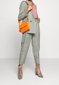 Abito scozzese di colore grigio chiaro con giacca aderente e pantaloni affusolati. Canotta corallo sotto, abbinata a una borsa arancione lucida e tacchi rosa con stampa pitonata.