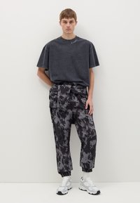 Camiseta de gran tamaño en gris oscuro con cuello redondo; pantalones cargo de rayas negro y gris; zapatillas deportivas blancas con detalles en gris.