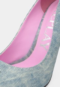 Γόβα από τζιν με μυτερή μύτη, ανοιχτό μπλε χρώμα, υφασμάτινη υφή και ροζ πάτο με ασημένια γράμματα.