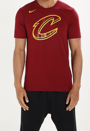 Camiseta de algodón roja con un gran logo "C" en amarillo y burdeos en el frente y un pequeño logo de Nike en la parte superior izquierda. Manga corta.