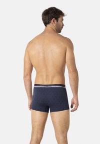 Un caleçon en coton bleu marine présente un motif géométrique texturé et une taille avec logo agrémentée d'une bande blanche contrastante. Vue arrière affichée.