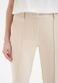 Beige op maat gemaakte broek van textuurstof, met een gladde tailleband, plat voorpand en subtiele zijnaaddetails.