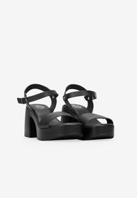 Sandalias de plataforma negras con tiras cruzadas, diseño de punta abierta y un tacón ancho. Fabricadas en material sintético suave.