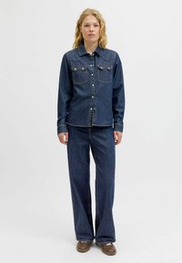 Denim srajca z western stilom, dvema žepoma na prsih in srebrnimi gumbi, v kombinaciji z širokimi denim hlačami v temnem pranju.