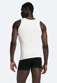 Hvid bomulds tanktop med ribbet tekstur, båret med sorte boxershorts, vist fra ryggen, der fremhæver pasformen og skulderdesignet.