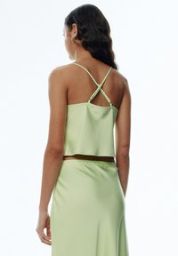 Satin crop top in light green, featuring thin crisscross straps and a loose fit, paired with a matching skirt. Smooth texture throughout.