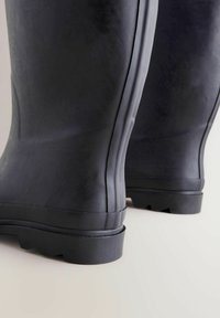 Zwarte rubberlaarzen met een gestructureerde afwerking, voorzien van geribbelde zijkanten en een stevige, gestructureerde zool. Het ontwerp is hoog en waterdicht.