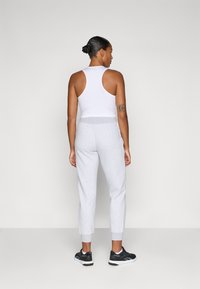 Top deportivo sin mangas blanco combinado con pantalones joggers grises de cintura elástica, con puños acanalados y zapatillas deportivas negras. Diseño sencillo, sin patrones.
