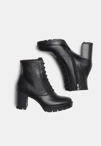Une paire de bottines en cuir noir avec des talons épais, un laçage à l'avant et des fermetures éclair sur les côtés, sur fond blanc.