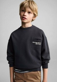 Črna trenirka iz bombaža s krožnim ovratnikom, dolgimi rokavi in sprednjim žepom, okrašena z belim napisom, v kombinaciji z oznako črtaste majice spodaj.