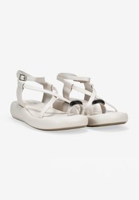 Sandali beige chiaro con tomaia sintetica liscia, caratterizzati da cinghie incrociate e un accento circolare nero sulla punta. Suola piatta.