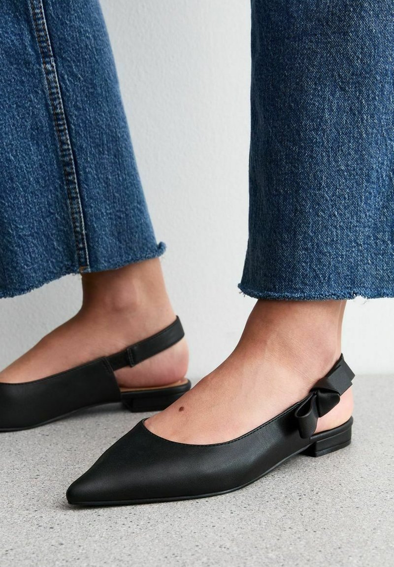 Svart läder slingback-lägenheter med spetsig tå, med en liten rosettdetalj vid hälen och låg profil. Texturerad svart yttersula.
